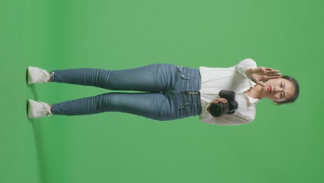 cuerpo lleno de fotógrafo asiático usando una cámara tomando fotos y haciendo señal de mano de parada mientras está de pie en el fondo de la pantalla verde en el estudio