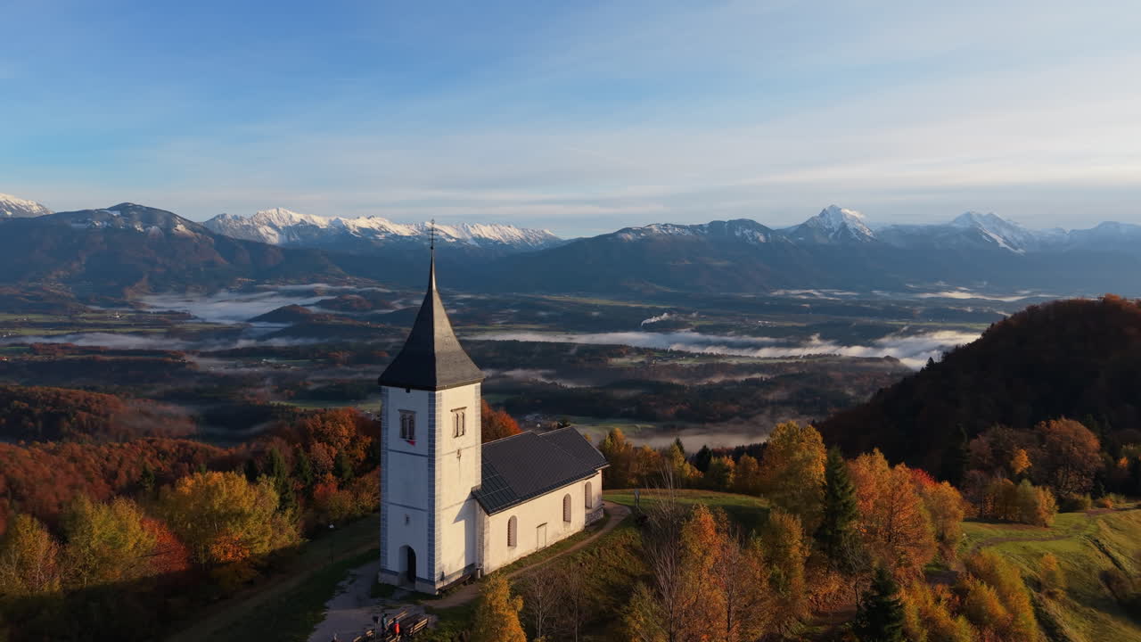 Beautiful aerial view of Saint Primus church on a hill in Jamnik, Slovenia with mountains and autumn colors