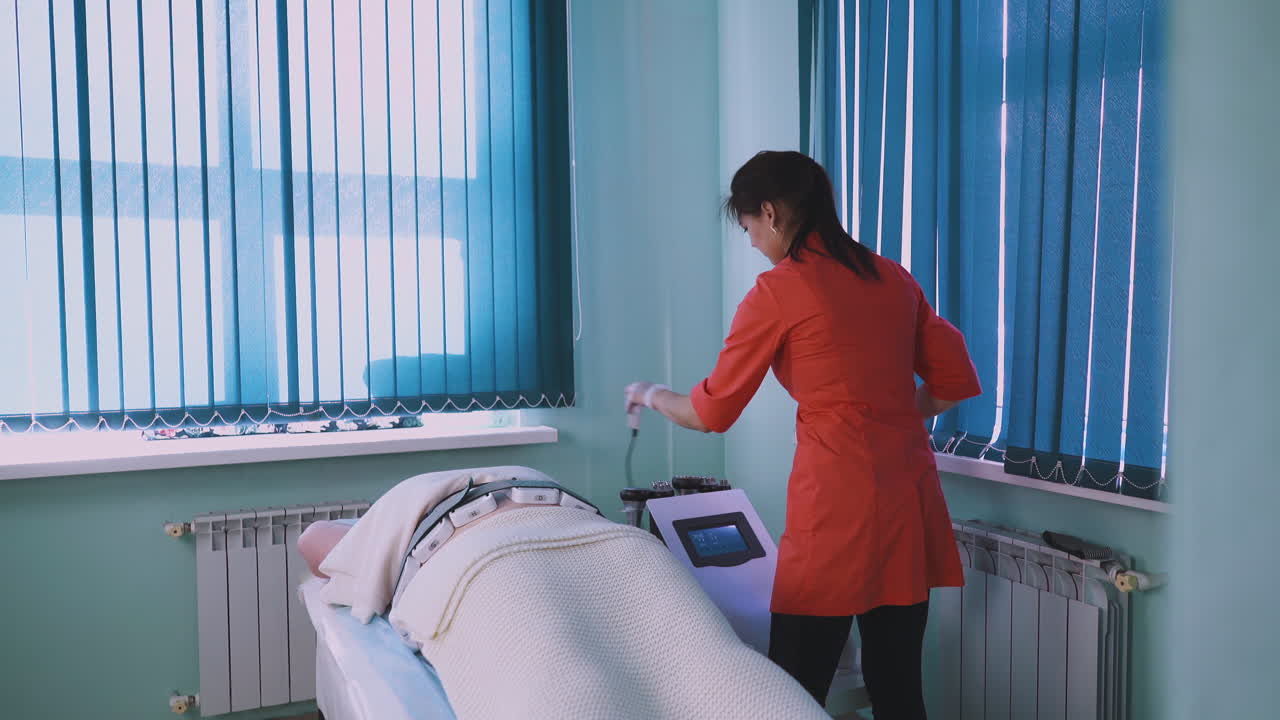 косметолог ставит электроды на живот девочки большого размера в клинике