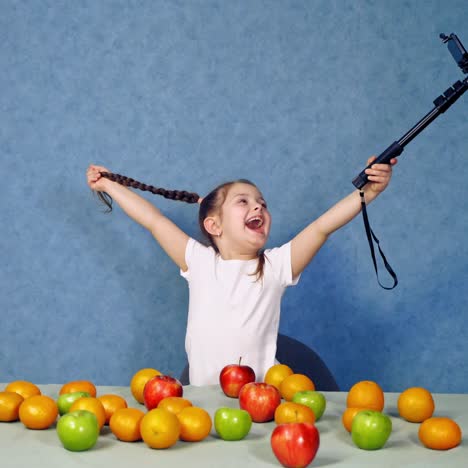 . girl making selfie with fruits. little girl having fun with fruits at table