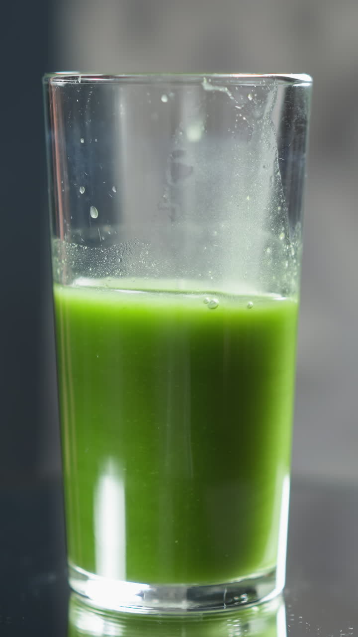 vaso de jugo de verduras verdes con tapa espumosa en la superficie reflectante, enfoque suave