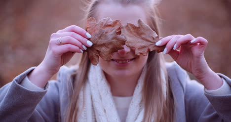 mujer sonriente escondiendo los ojos con hojas en otoño 2