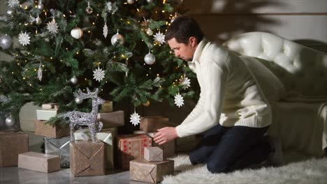 man preparing christmas gifts under a decorated christmas tree