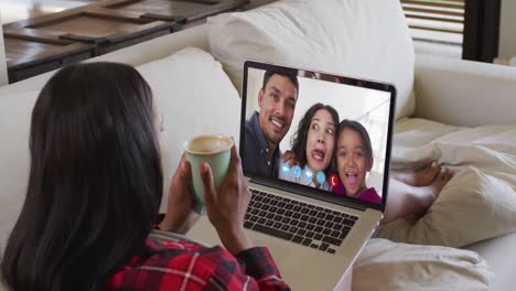 Mixed-race-woman-sitting-on-sofa-using-laptop-making-video-call-with-male-friends