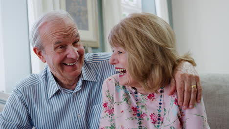 Portrait-Of-Smiling-Senior-Couple-Sitting-On-Sofa-At-Home