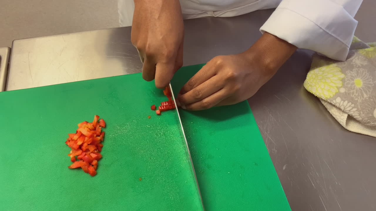 Hands of young chef in kitchen dicing sweet red bell pepper with knife