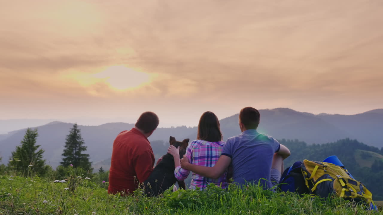 개를 데리고 있는 관광객 두 명이 땅에 앉아 산의 아름다운 경치를 감상한다