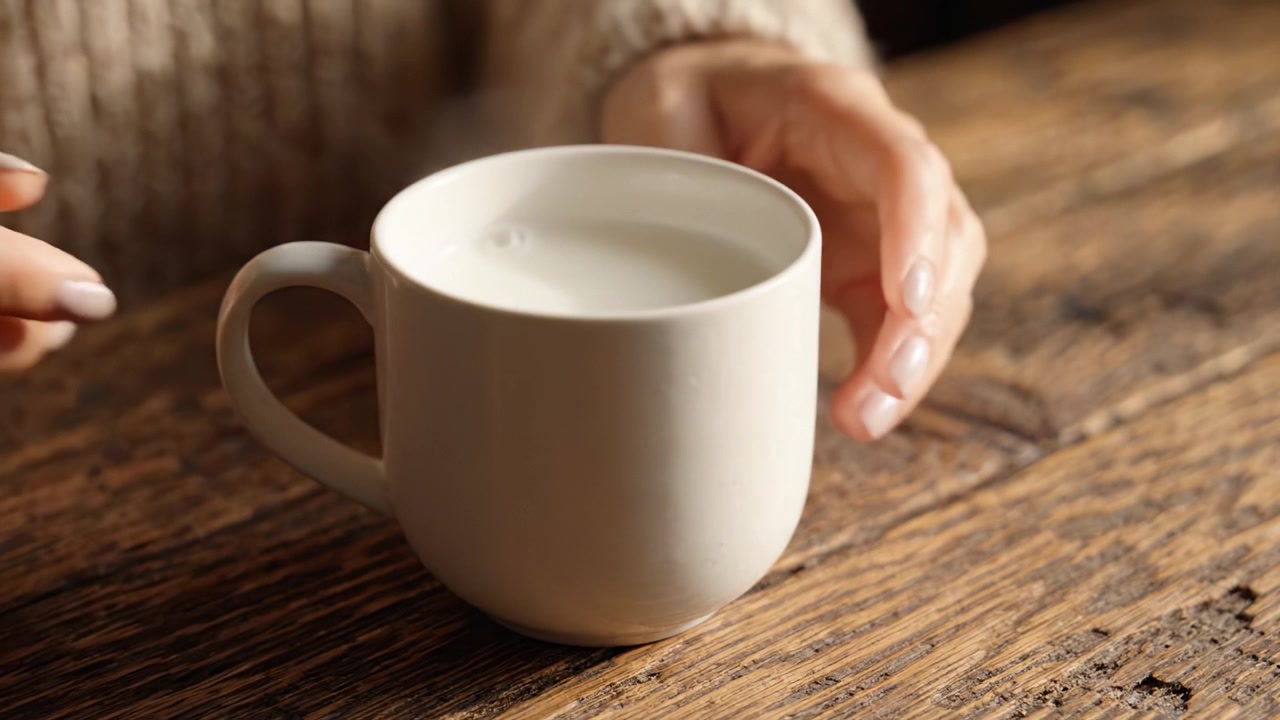 Un momento delicato catturato: Una mano che tiene una tazza bianca di bevanda rinfrescante appoggiata su un tavolo di legno rustico con calde texture.