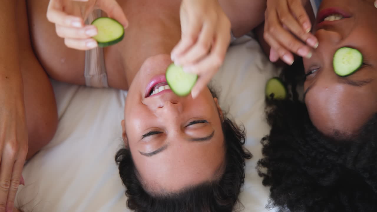 Laughing Diverse female friends relaxing with cucumber slices during spa day at home