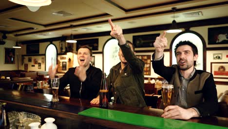 tres aficionados al fútbol están viendo el partido en un bar deportivo, animando y celebrando goles con cerveza. los hombres son muy emocionales, gritando y gestando.