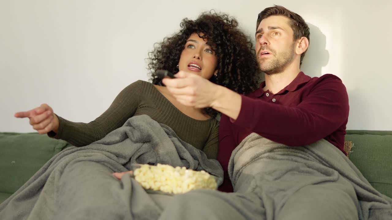 Multietnisk par, der skifter kanal på tv med fjernbetjening