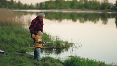 little-boy-is-fishing-on-shore-of-lake-grandfather-is-teaching-his-grandson