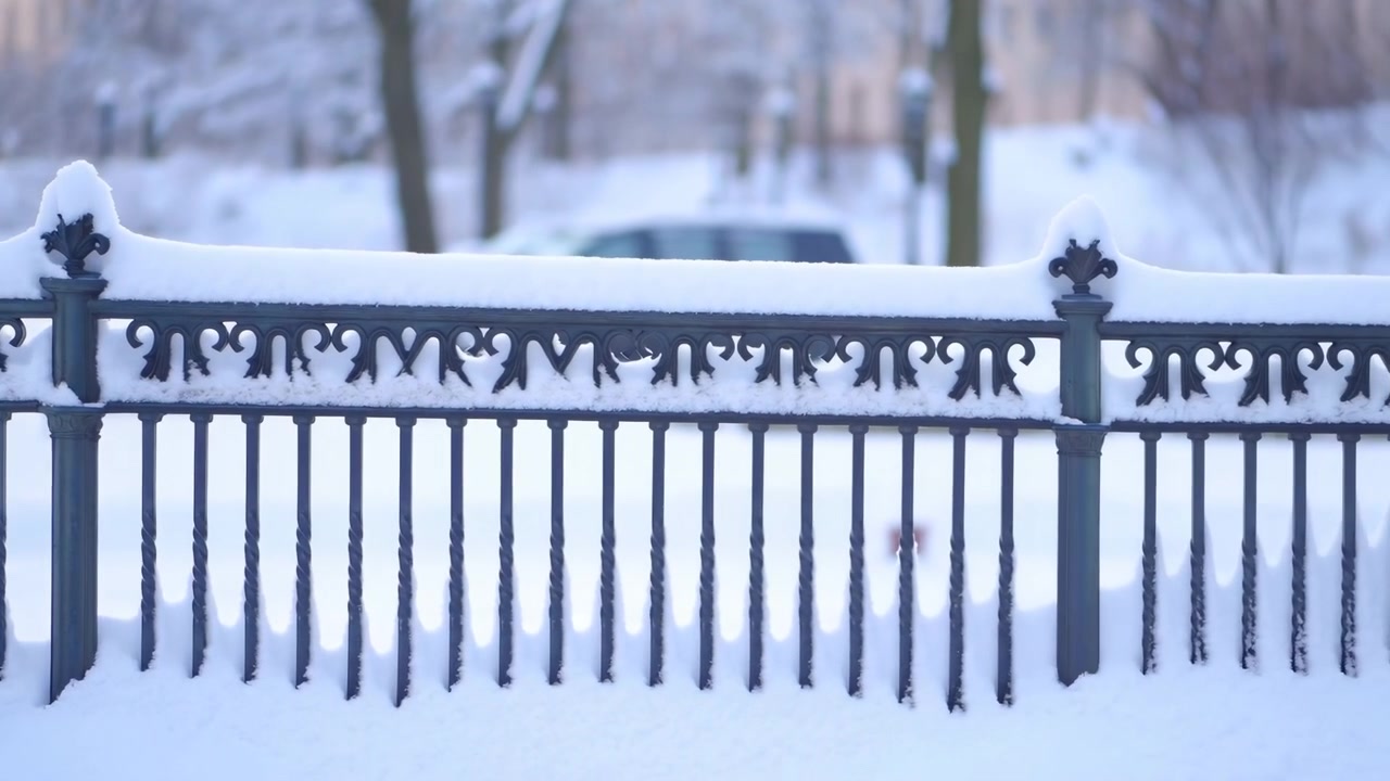 Vista panoramica all'altezza degli occhi di una recinzione in ferro battuto ornata, coperta di neve fresca, in un parco urbano, con ringhiera decorativa, copripali arrotondati, balaustri, luce invernale soffusa e un'atmosfera stagionale calma.