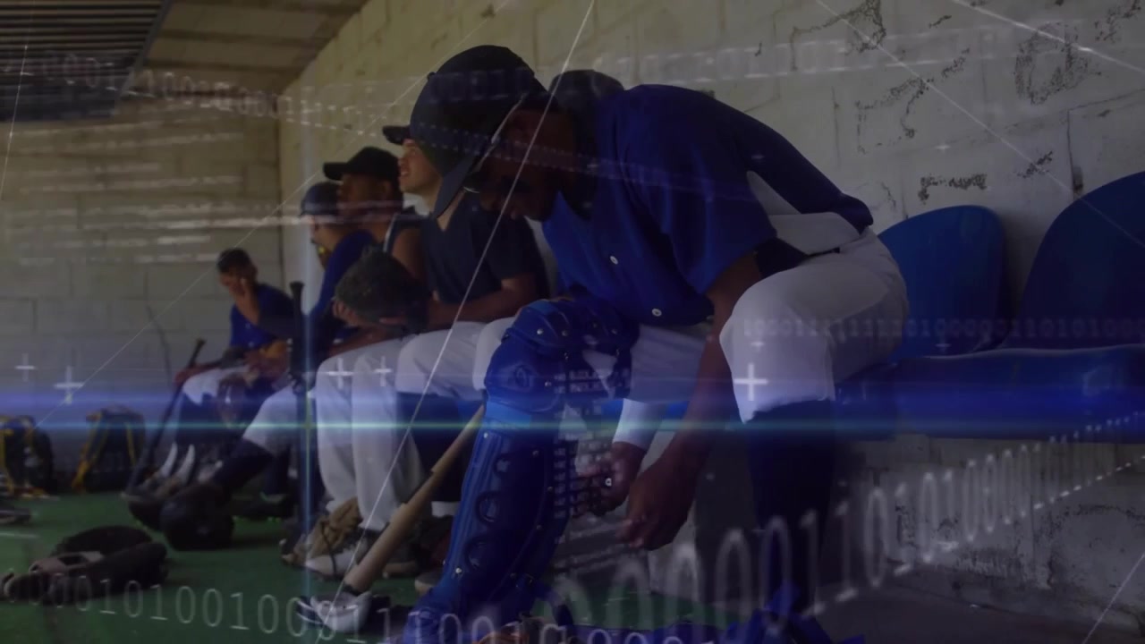 Camera panning onto catcher fastening strap in dugout, teammate inspecting bat before baseball play