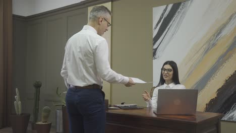 male employee giving document to his boss, shaking hands with her and then leaving