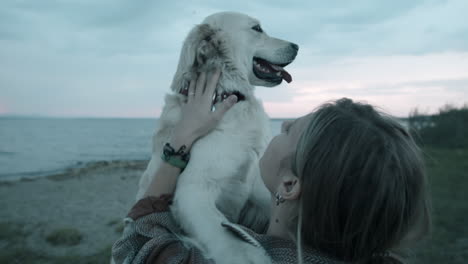 woman petting lovely golden retriever on lakeshore in evening