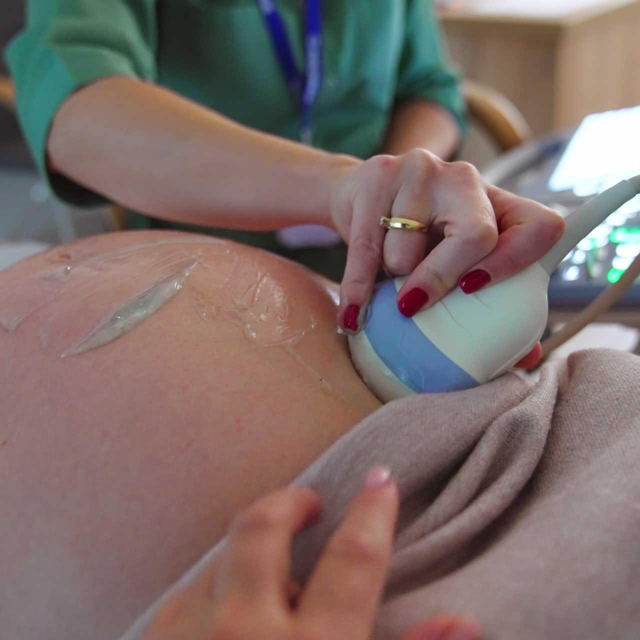 Device is moved by the big pregnant belly for ultrasound diagnostics. Doctor sitting at apparatus at backdrop in blur