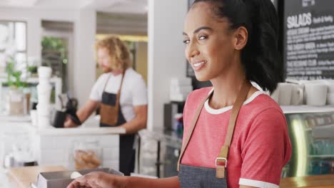 Portrait-of-happy-biracial-female-barista,-smiling-behind-the-counter-in-cafe