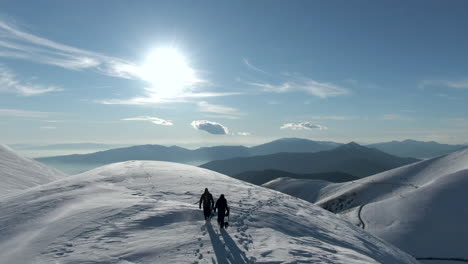 two snowboarders walking out towards peak of mountain with snowboards in hand