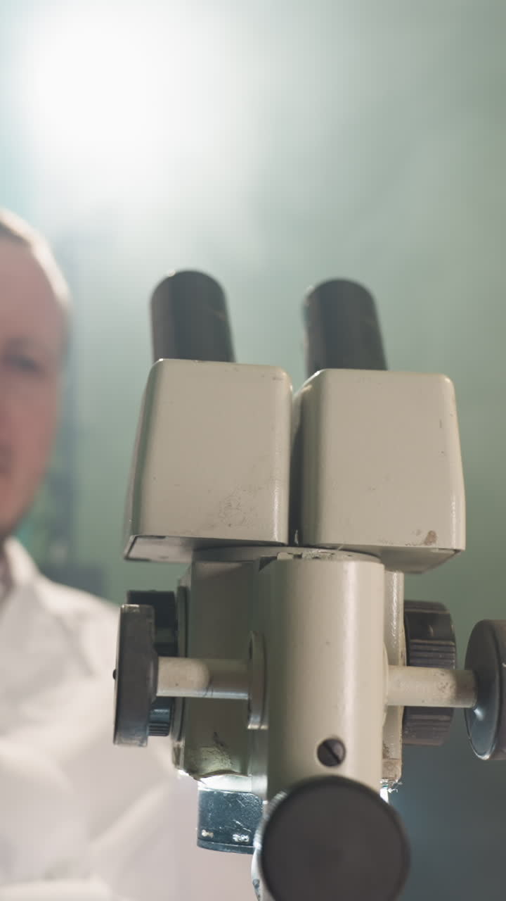 una vista ravvicinata di uno scienziato che esamina intensamente i campioni attraverso un microscopio in un laboratorio, poi si allontana dal microscopio, lo scienziato è a fuoco, indossa un cappotto bianco da laboratorio