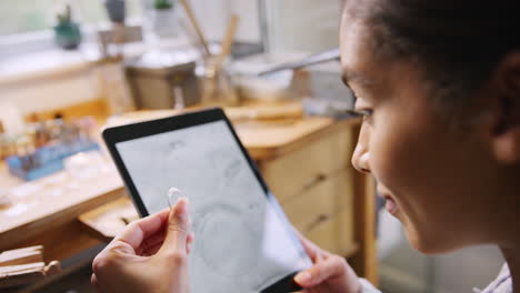 Female-Jeweller-Comparing-Ring-With-Drawn-Design-On-Digital-Tablet-In-Studio