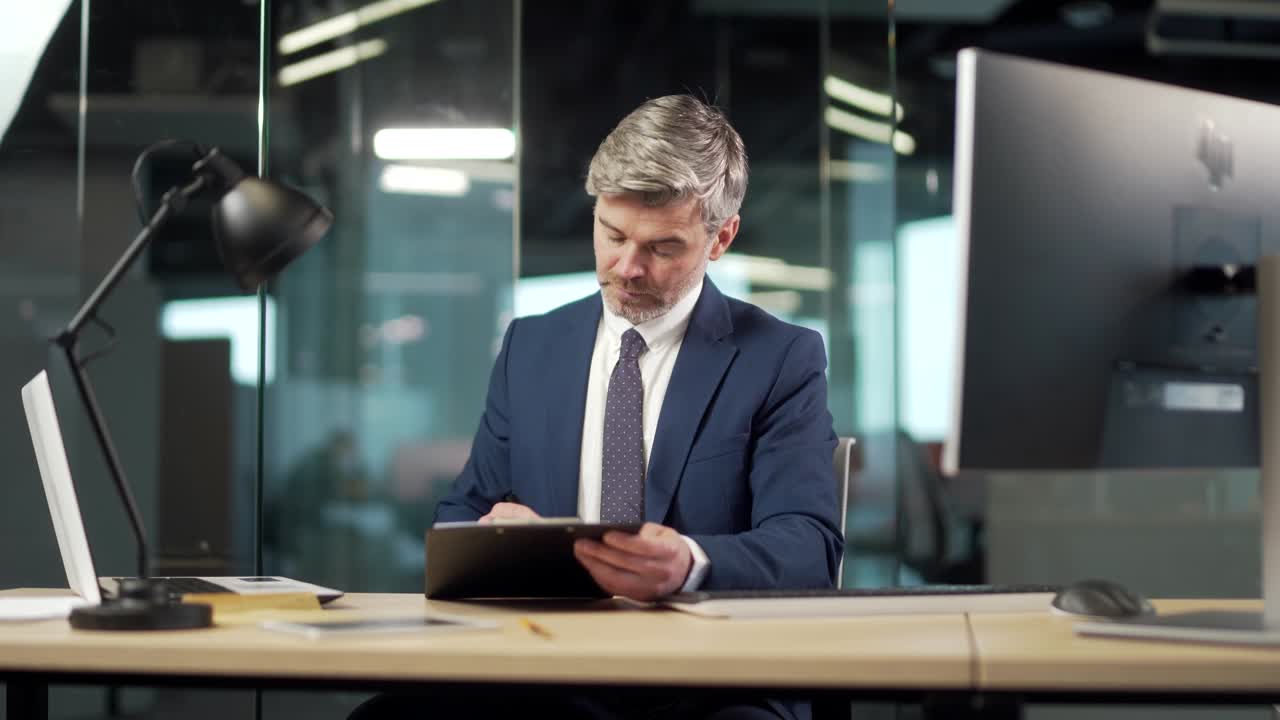 Senior business man signs a approval document in the office. Mature gray successful banker or lawyer businessman reading and signing business partnership contract