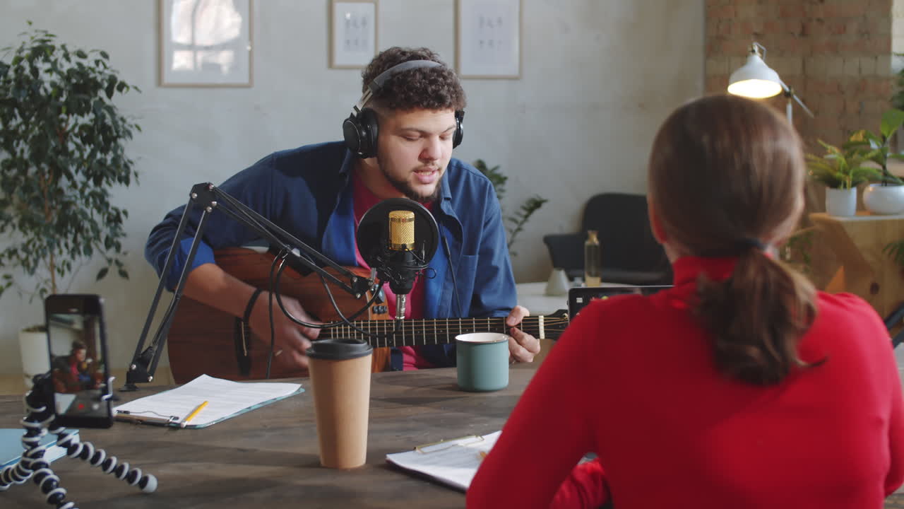 Uomo che canta e suona la chitarra in uno studio di registrazione con una conduttrice.