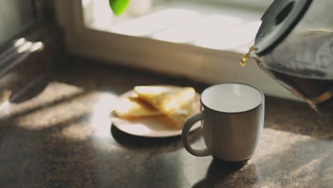 Coffee-Is-Poured-Into-A-White-Mug-Next-To-Garlic-Bread-On-Plate