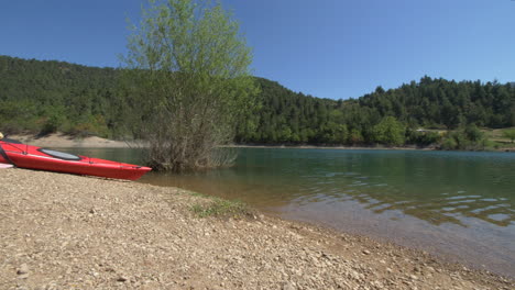 pan from red kayaks on stone beach along tsivlou lake in greece