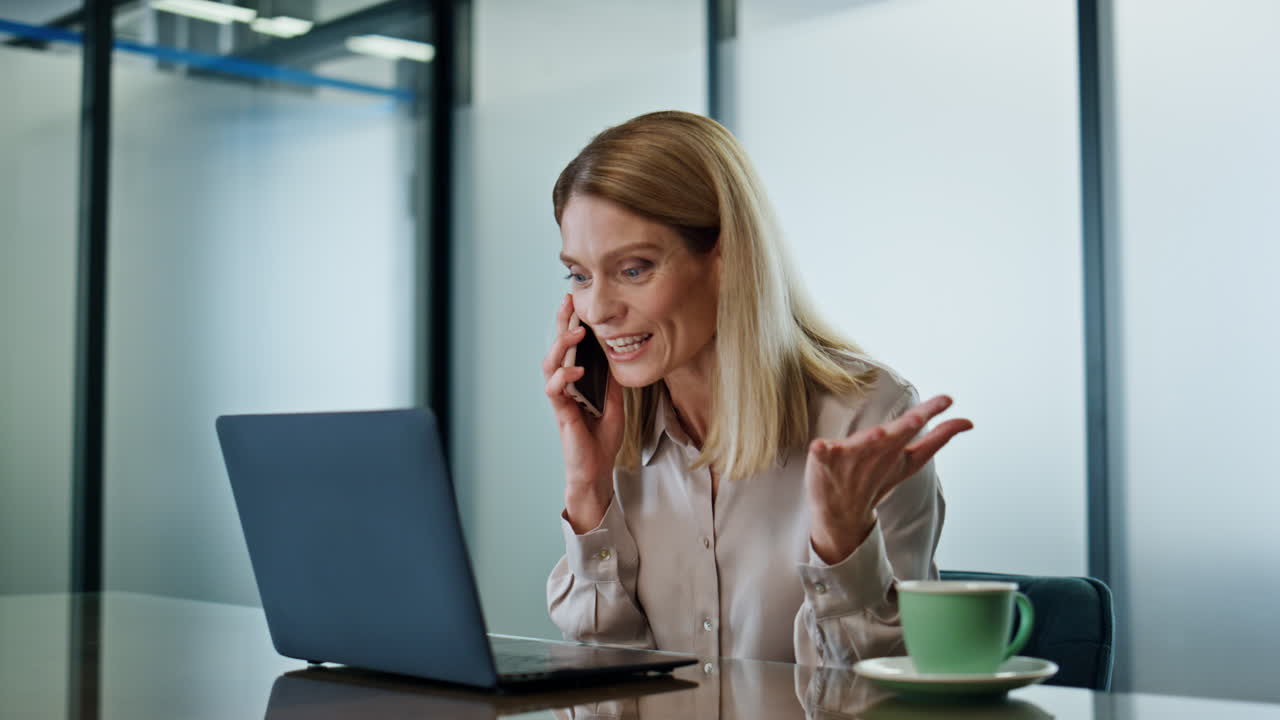 Primo piano di una donna entusiasta che si rallegra per una chiamata sullo smartphone in ufficio. La direttrice parla al telefono.