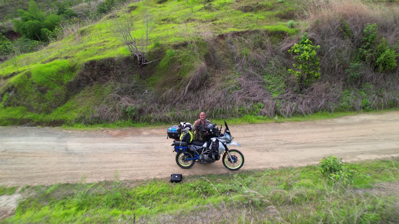 motorcyclist stopped on dirt road through a green, mountainous landscape, off road travel