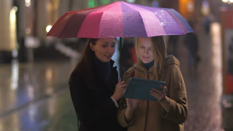 amigas con tableta bajo un paraguas