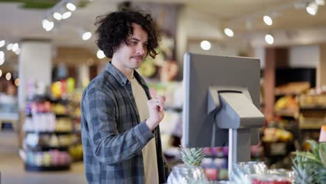 A-guy-with-curly-hair-and-a-mustache-in-a-plaid-shirt-weighs-a-pineapple-on-a-scale-in-a-supermarket