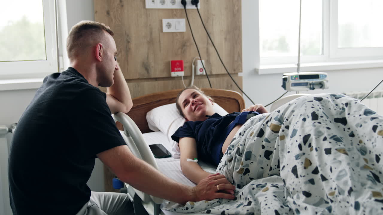 Man is holding his pregnant wife's hand while she's tested on the medical equipment. Diagnostics and fetal heart monitoring before the labor.