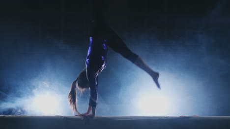 the girl performs a trick on a log in backlight and slow motion in sports gymnastic clothing. smoke and blue. jump and spin on the balance beam