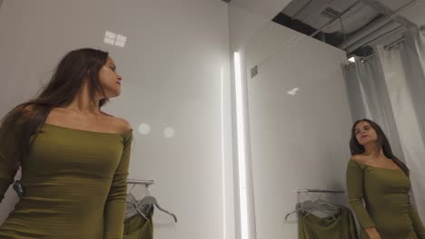 a woman examines her outfit in a changing room, adjusting her clothes while looking at her reflection in the mirror.