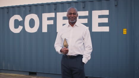 portrait of male freight haulage manager with digital tablet by shipping container for coffee