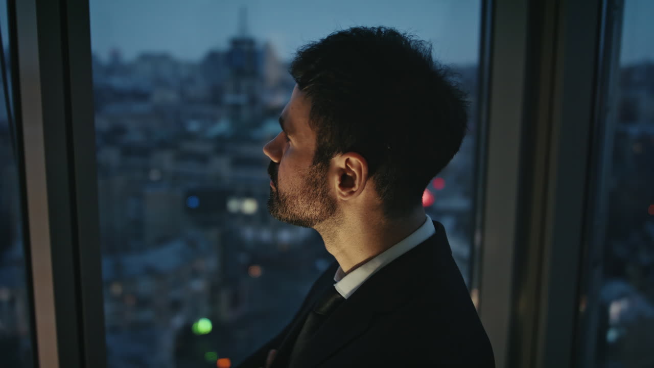 trabajador corporativo de pie en la oficina nocturna mirando la ventana de cerca. hombre de negocios cansado