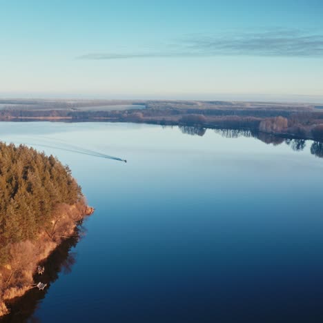 calm lake in the evening. boat moving on the river at sunset. beautiful nature background. trees reflected in water. aerial view.