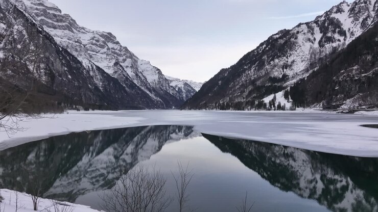 Partially frozen Klöntalersee lake reflecting Swiss Alps in Klöntal, Glarus, Switzerland