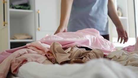 woman tidying up a pile of clothes on a bed.
