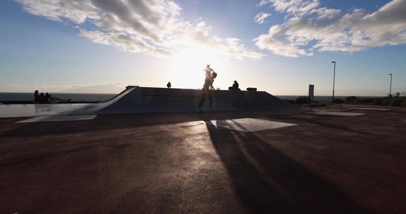 Silhouette di uno skateboarder contro il cielo dorato del tramonto allo skatepark