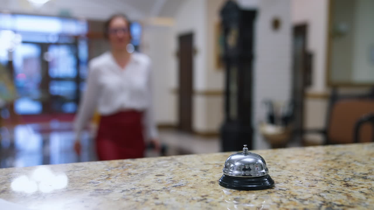 Reception lobby. Bell button on a reception table on blur background of a hotel. Lady pressing the metal bell on desk to call a receptionist in hotel. Close-up.