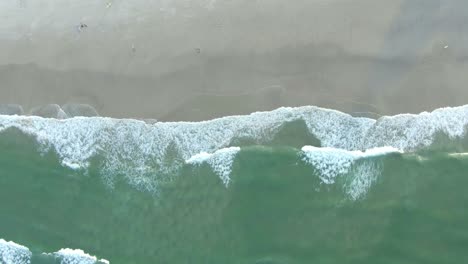 aerial spinning drone view of sea waves breaking on sandy coastline