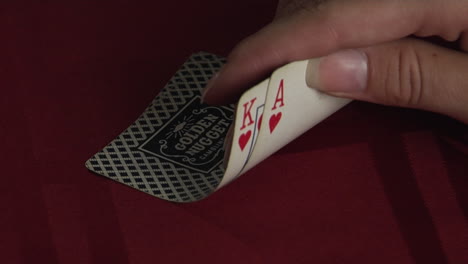 a hand turns up the corner of two playing cards to reveal a king and an ace