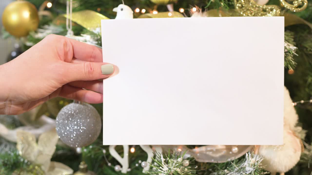 la mano sostiene una nota de tarjeta de papel blanco frente al hermoso árbol de navidad decorado
