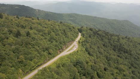 car drives up lush forest highway to smoky mountain summit ridge