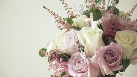 slow motion ascending shot of a wedding bouquet with various flowers with pink and yellow roses, decorations and bows against a white background