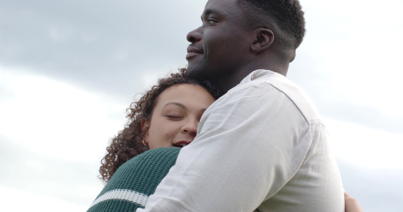 Coppia afroamericana che si abbraccia all'aperto, la donna con maglione verde nasconde il viso, l'uomo la conforta
