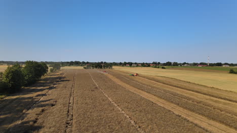 Vuelo-De-Avance-Aéreo-Que-Muestra-La-Cosecha-De-Tractores-Cosechando-Tierras-De-Cultivo-Durante-El-Cielo-Azul